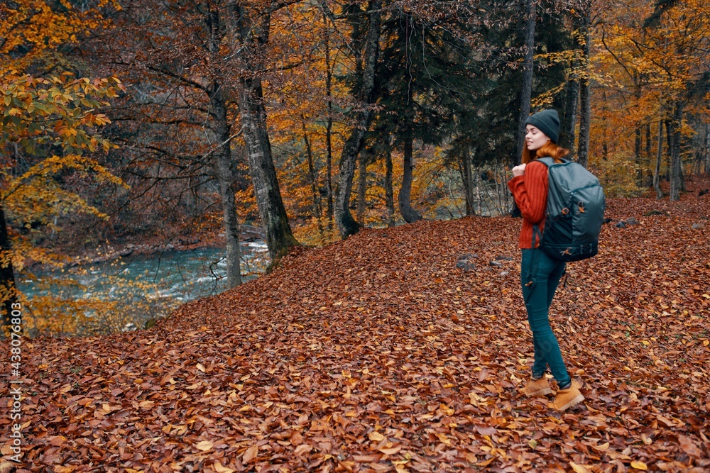 woman in autumn in the park with fallen leaves and a backpack on her back river in the background