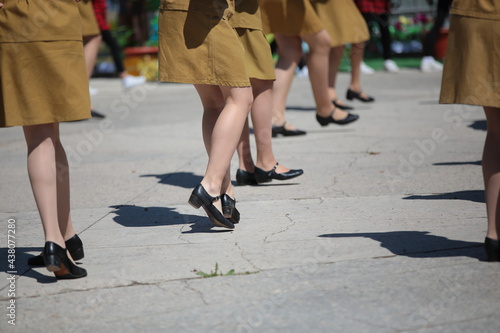 Image of a group of female legs in black shoes and a short soldier's skirt dancing a step at an open-air parade in the square on a summer day.Woman dancer in camouflage clothes.Background