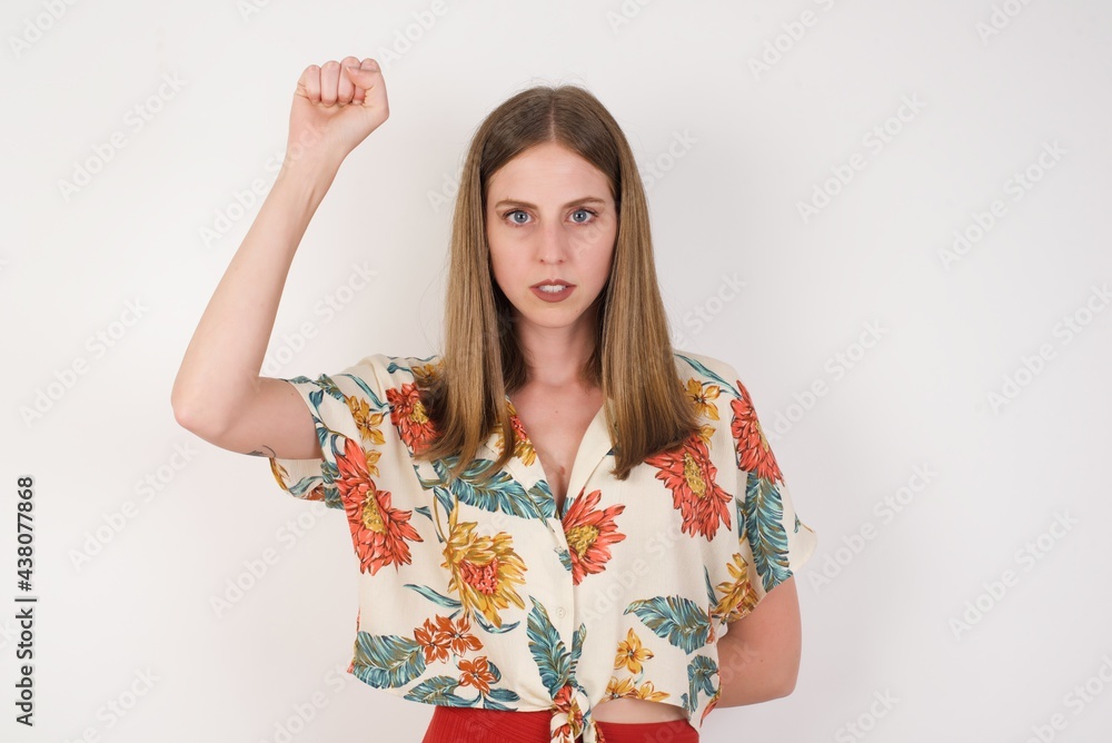 Young pretty woman feeling serious, strong and rebellious, raising fist up, protesting or fighting for revolution against white wall. Young pretty woman feeling serious, strong and rebellious, raising fist up, protesting or fighting for revolution against white wall.