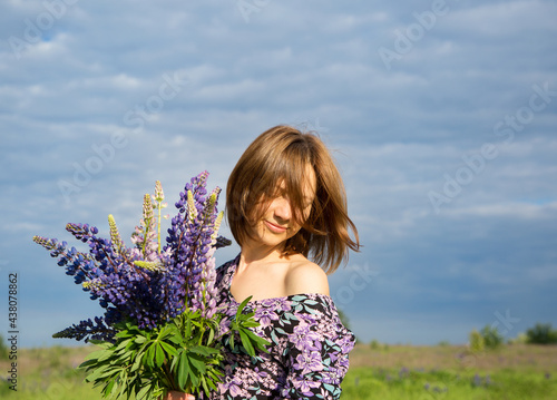 Happy woman's face covered with hair against blue sky. In the hands of a bouquet of wild flowers. atmospheric photo, flowering season, carefree day. digital detox, enjoyment of nature, joy of moment