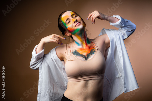 Girl with smears of paint on her face in a white shirt dancing on an orange background photo