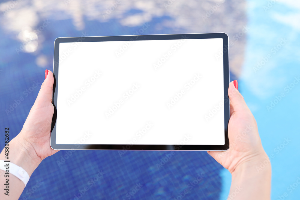 Female hands hold tablet with blank white screen above pool water