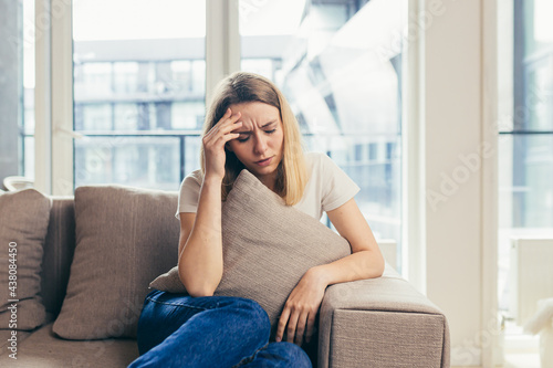 Portrait young woman sitting on sofa at home depressed. Girl is having a hard time with stress. Caucasian female indoors alone worried about problems. unhappy blonde student in living room or bedroom 