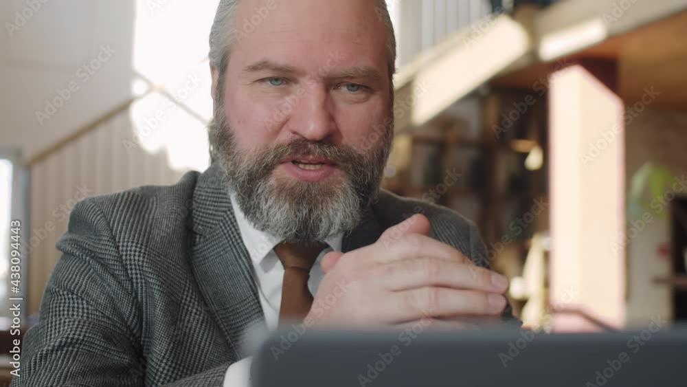 Senior Caucasian businessman in formal suit sitting in restaurant, smiling and speaking on video call on laptop Senior Caucasian businessman in formal suit sitting in restaurant, smiling and speaking on video call on laptop