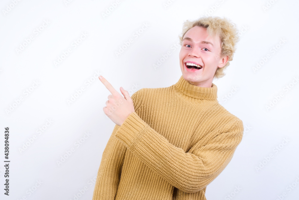 Young handsome Caucasian blond man standing against white background pointing away and smiling to you. Look over there! Young handsome Caucasian blond man standing against white background pointing away and smiling to you. Look over there!
