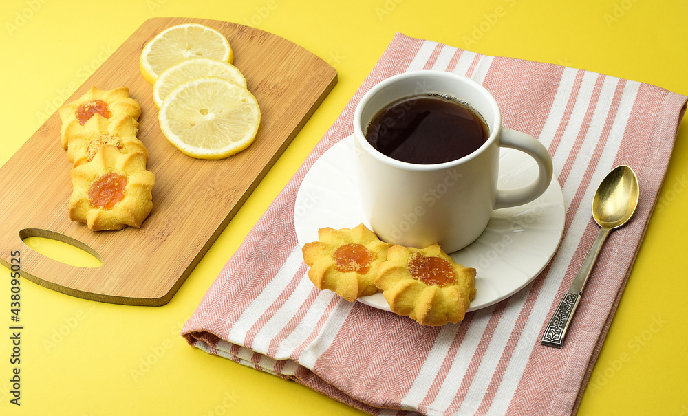 White cup of tea, homemade cookies, sliced lemon, kitchen napkin, tea spoon. Afternoon, dessert, tea party concept. Side and top view. White cup of tea, homemade cookies, sliced lemon, kitchen napkin, tea spoon. Afternoon, dessert, tea party concept. Side and top view.