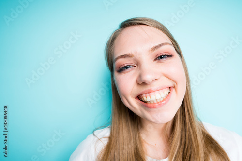Happy girl with long hair smiling broadly looking at the camera while standing on a blue background