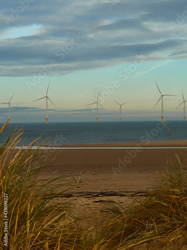 Fototapeta Naklejka Na Ścianę i Meble -  The near-shore wind farm at Redcar with a foreground of dune grass, sandy beach and the sea. The turbines stand on the horizon before a winter sky.