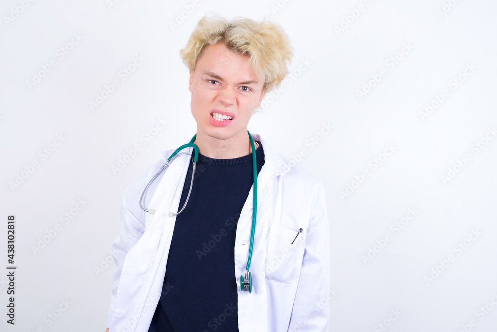 Mad crazy young handsome Caucasian doctor man standing against white background clenches teeth angrily, being annoyed with coming noise. Negative feeling concept. Mad crazy young handsome Caucasian doctor man standing against white background clenches teeth angrily, being annoyed with coming noise. Negative feeling concept.