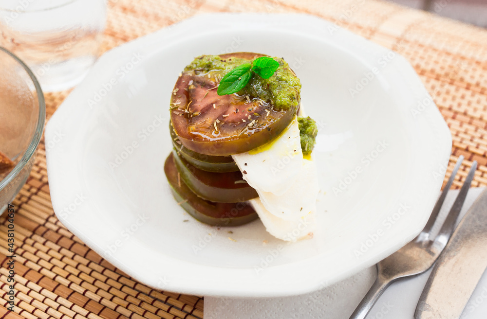 caprese salad with mozzarella, black tomatoes and pesto in white plate caprese salad with mozzarella, black tomatoes and pesto in white plate