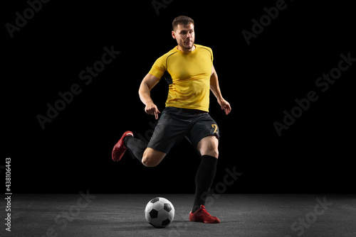 Powerful, flying above the field. Young football, soccer player in action, motion isolated on black studio background . © master1305