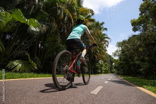 Woman riding a bike on tropical park trail in summer
