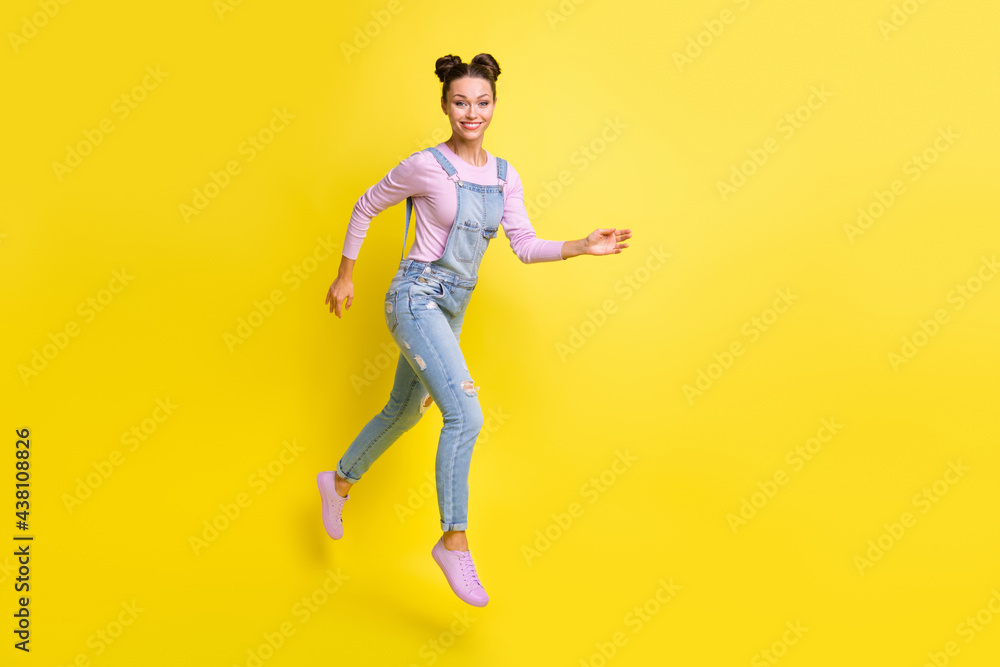Photo of cheerful lovely lady jump run beaming white smile wear jeans overall shoes isolated yellow background