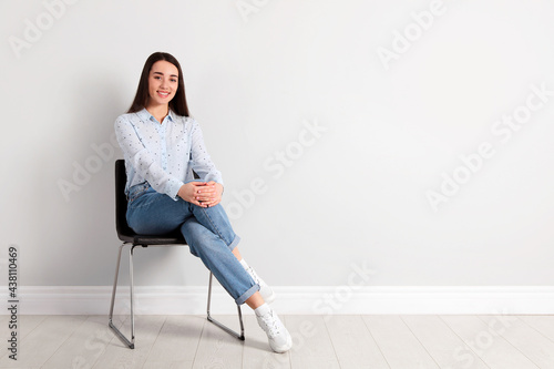 Canvastavla Young woman sitting on chair near white wall in office, space for text