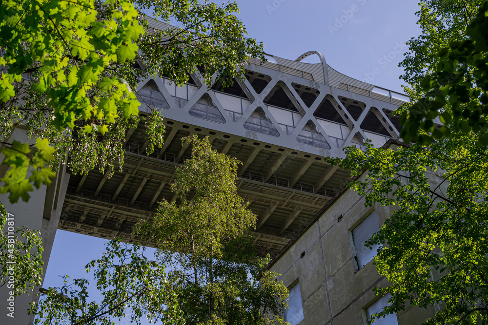 View of detail of highway bridge from below against the blue sky. The road passing over the green trees of the city. Saint Petersburg, Europe View of detail of highway bridge from below against the blue sky. The road passing over the green trees of the city. Saint Petersburg, Europe