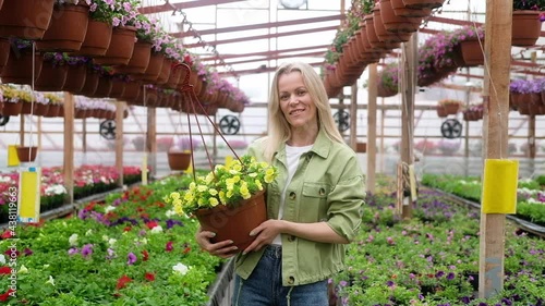 Close-up portrait of Woman gardener holding potted flowers in a greenhouse. Flower shop. female farmer takes care of the growing plants in the greenhouse. Florist in the garden center, flower business
