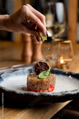 Woman is squeezing a slice of lime on a fish tartar in a posh restaurant, young beautiful woman hands photo