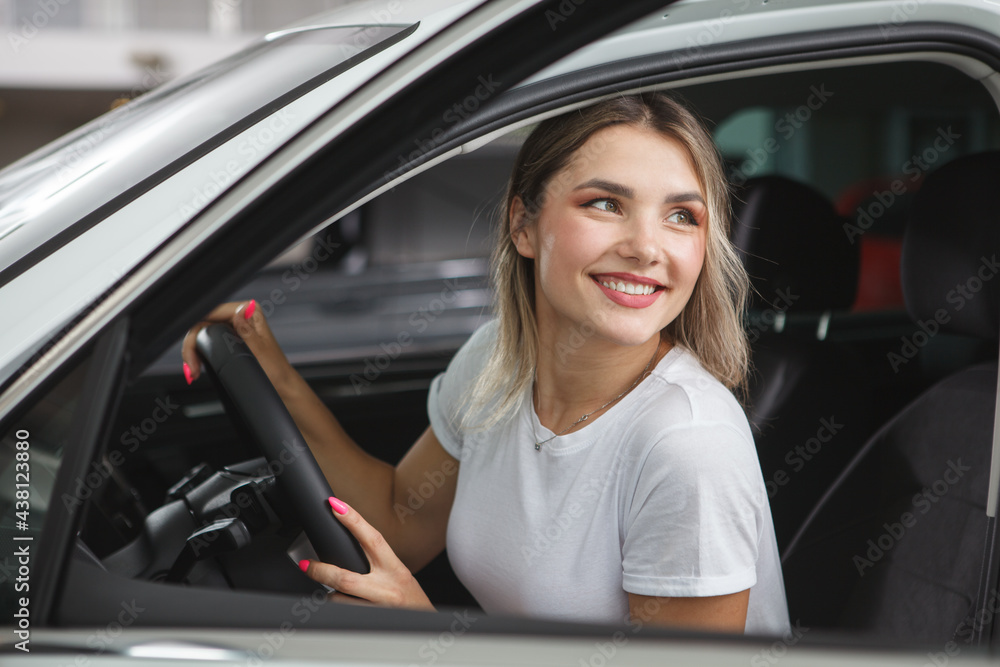 Excited beautiful woman sitting in a new automobile at car dealership
