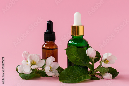Serum glass bottles with pipette and beautiful flowesr on the pink background. Natural Organic Spa Cosmetic concept. Front view.