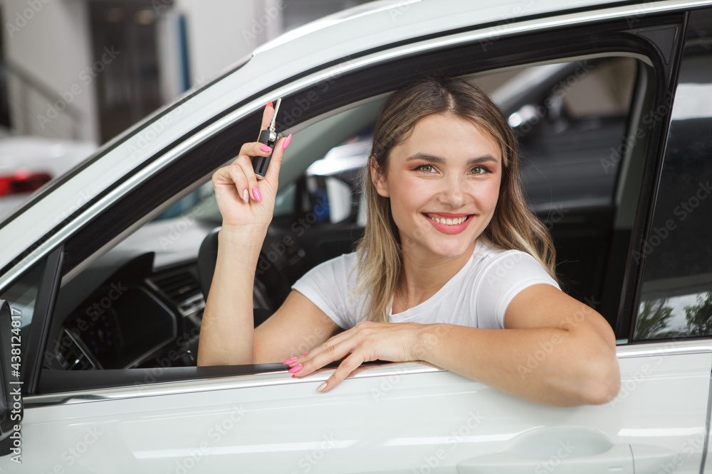 Beautiful cheerful woman holding car keys, sitting in her new automobile