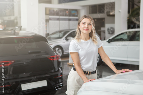 Young woman choosing new auto to buy at car dealership, copy space