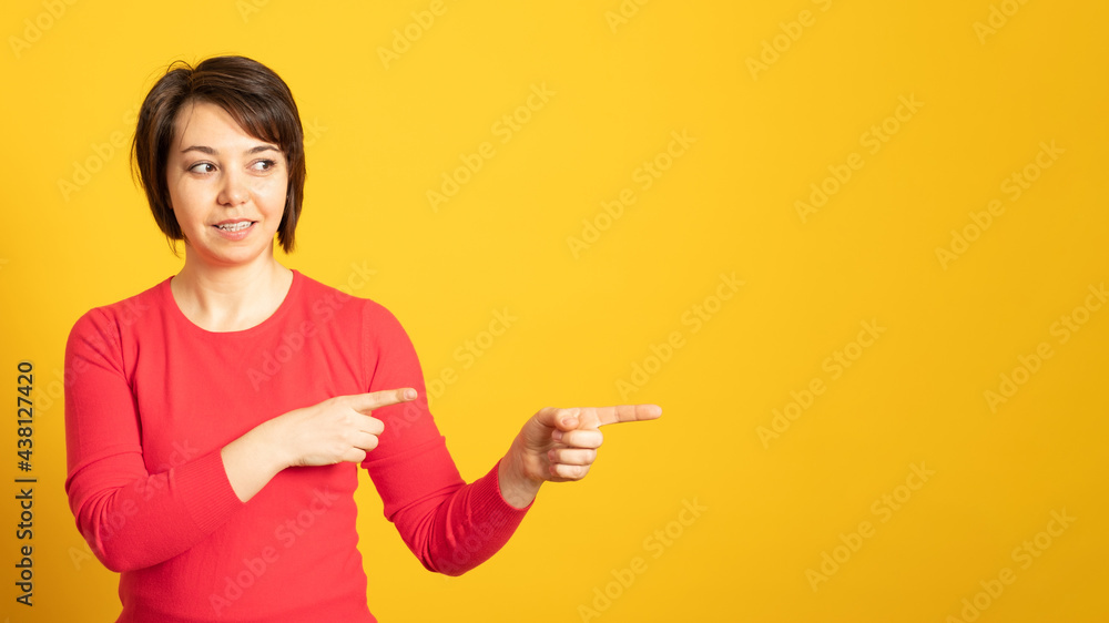 Banner. Pleased woman points away with both fore fingers, shows blank space for your promotion, isolated over yellow background. People, advertisement concept. Banner. Pleased woman points away with both fore fingers, shows blank space for your promotion, isolated over yellow background. People, advertisement concept.
