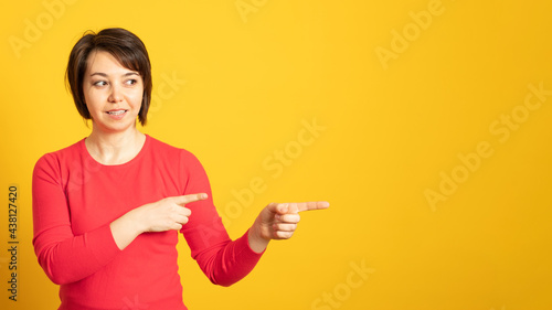 Banner. Pleased woman points away with both fore fingers, shows blank space for your promotion, isolated over yellow background. People, advertisement concept.