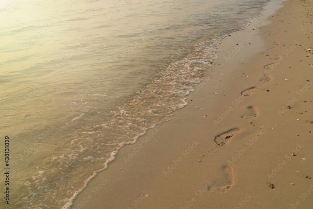 Soft focus of the waves beat at the beach with sand, footprints and reflection of sunlight on water in summer morning. Nature background concept.