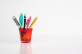 Different colorful pens in a red stained-glass cup isolated on white front view studio shot