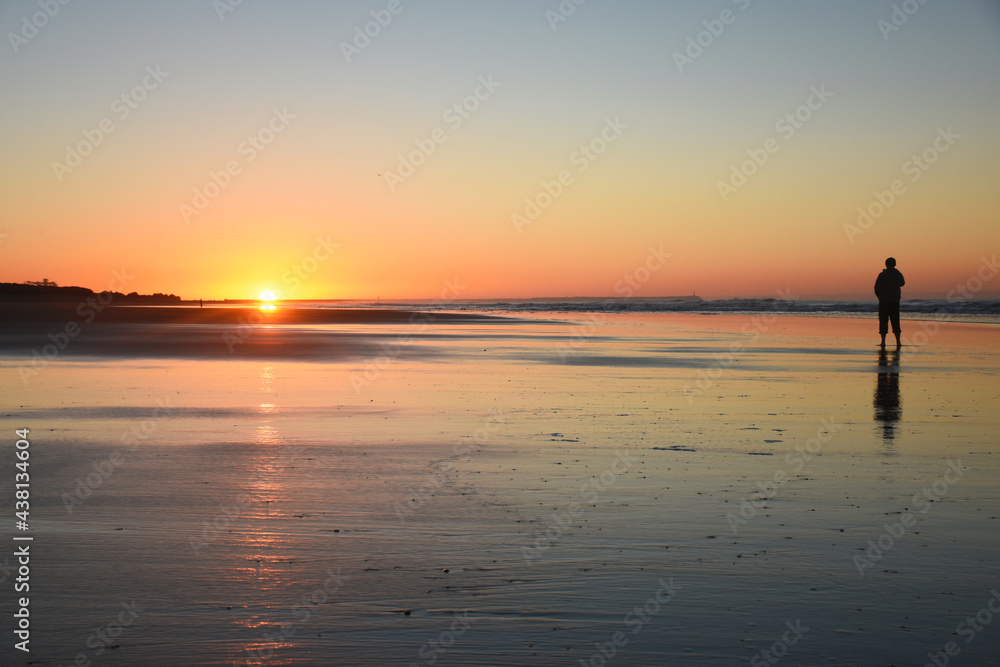 Man watching the sunrise on the beach, with warm tones and a beautiful reflection of the sunlight in the water