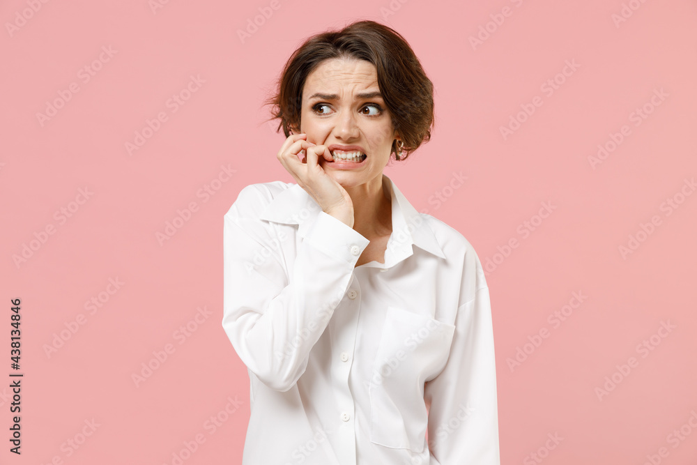 Young puzzled confused troubled thoughtful employee business woman corporate lawyer in classic formal white shirt work in office look aside biting nail fingers isolated on pastel pink color background Young puzzled confused troubled thoughtful employee business woman corporate lawyer in classic formal white shirt work in office look aside biting nail fingers isolated on pastel pink color background
