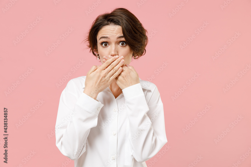 Young shocked impressed surprised amazed confused employee business woman corporate lawyer in classic formal white shirt work in office cover mouth with arms isolated on pastel pink color background Young shocked impressed surprised amazed confused employee business woman corporate lawyer in classic formal white shirt work in office cover mouth with arms isolated on pastel pink color background