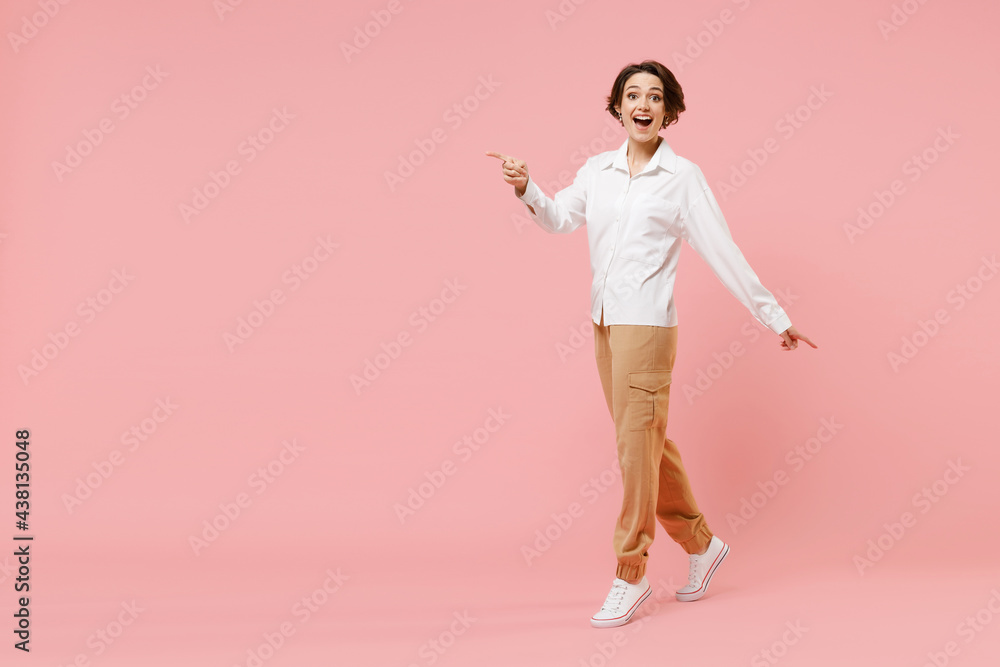 Full length surprised young employee business woman corporate lawyer in classic formal white shirt work in office point index finger aside on workspace area mock up isolated on pastel pink background. Full length surprised young employee business woman corporate lawyer in classic formal white shirt work in office point index finger aside on workspace area mock up isolated on pastel pink background.