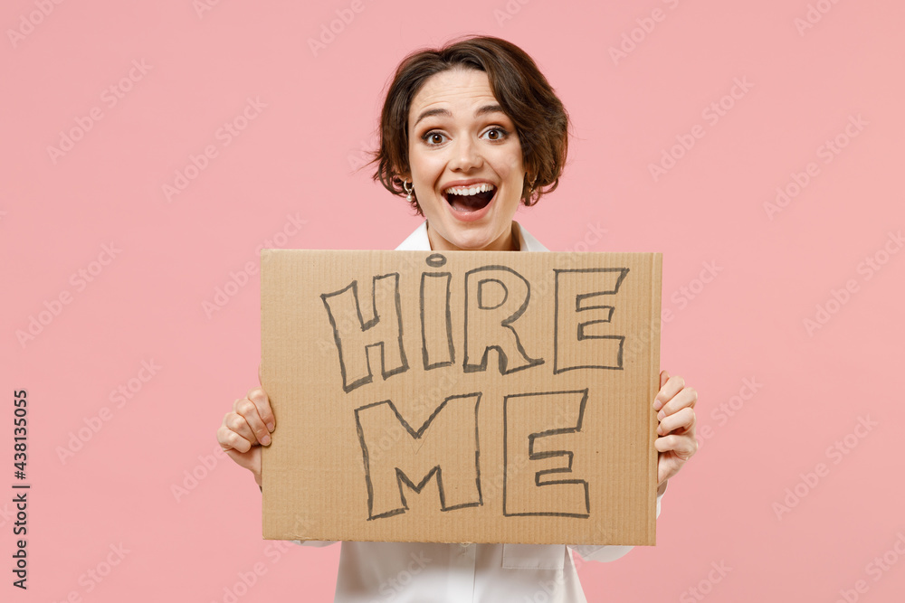 Young fun smiling employee business secretary woman corporate lawyer in classic formal white shirt work in office hold cardboard sign card need job isolated on pastel pink background studio portrait. Young fun smiling employee business secretary woman corporate lawyer in classic formal white shirt work in office hold cardboard sign card need job isolated on pastel pink background studio portrait.