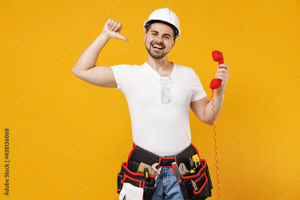 Young employee handyman man in protective helmet hardhat point finger himself speak by handset phone isolated on yellow background Instrument accessories renovation apartment room Repair home concept Young employee handyman man in protective helmet hardhat point finger himself speak by handset phone isolated on yellow background Instrument accessories renovation apartment room Repair home concept