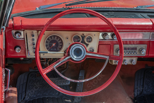 Close up view of a 1960s retro red convertible. Interior shot of the steering wheel and dashboard, including the push button automatic transmission.