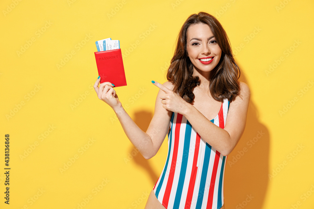 Happy young woman slim body wear striped red blue swimsuit hold passport boarding pass ticket isolated on vivid yellow color background studio Summer hotel pool sea rest sun tan air flight concept Happy young woman slim body wear striped red blue swimsuit hold passport boarding pass ticket isolated on vivid yellow color background studio Summer hotel pool sea rest sun tan air flight concept