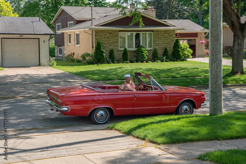 Older man driving his vintage red 1960s convertible in reverse down a residential street.