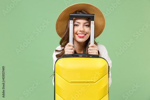 Close up satisfied cool traveler tourist woman in casual clothes hat hiding with yellow suitcase valise isolated on green background Passenger travel abroad weekend getaway Air flight journey concept