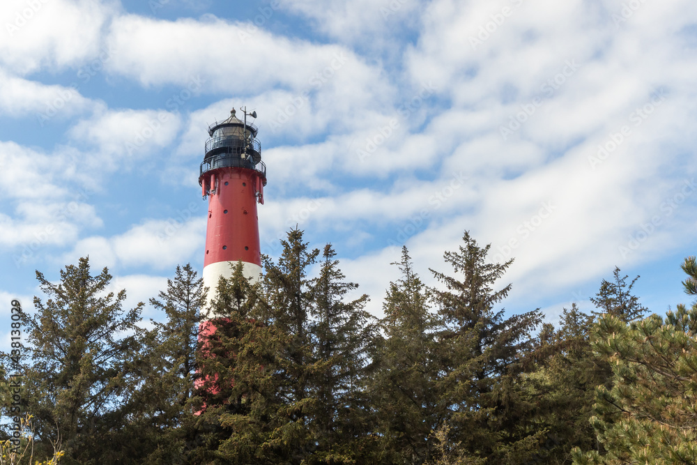 a red and white striped lighthouse stands on a dune, in the foreground you can see beach grass growing. a lighthouse stands against a bright blue sky with light white veil clouds. a red and white striped lighthouse stands on a dune, in the foreground you can see beach grass growing. a lighthouse stands against a bright blue sky with light white veil clouds.