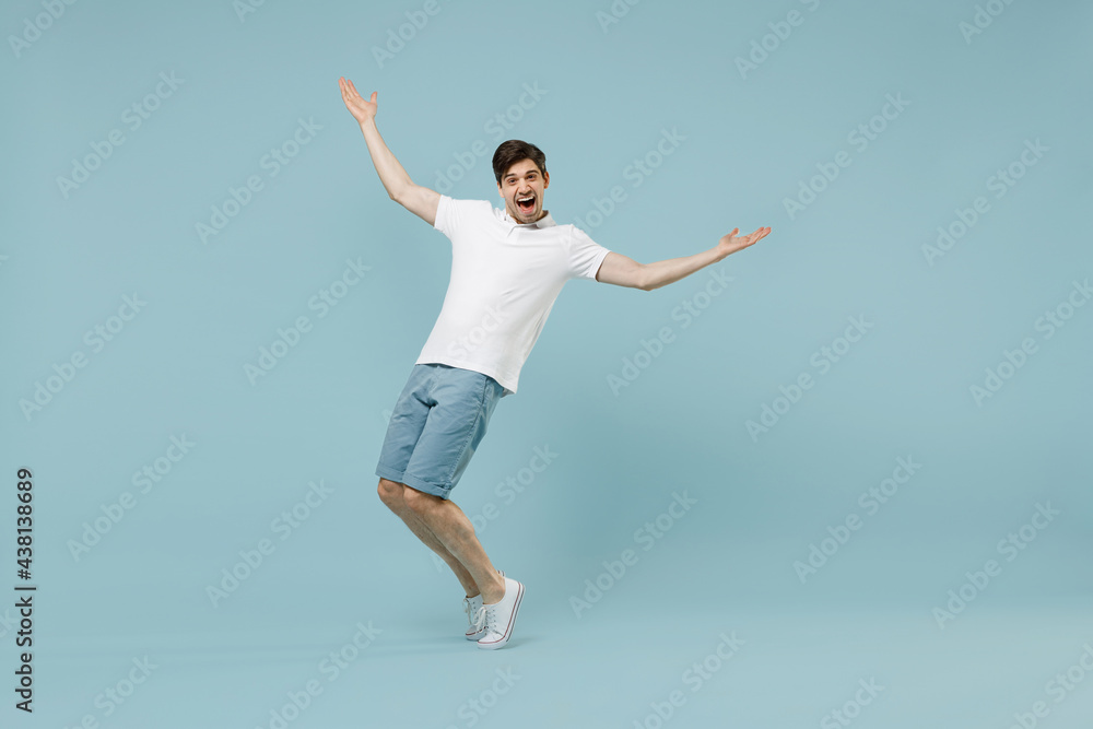 Full length young fun man 20s wearing white basic t-shirt stand with outstretched hands leaning back stand on toes isolated on pastel blue color background studio portrait. People lifestyle concept. Full length young fun man 20s wearing white basic t-shirt stand with outstretched hands leaning back stand on toes isolated on pastel blue color background studio portrait. People lifestyle concept.