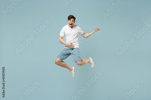 Full length singer rock musician young fun happy man 20s wear white casual basic t-shirt jumping high play guitar isolated on pastel blue color background studio portrait. People lifestyle concept