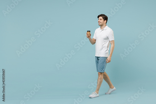 Full size young happy fun man in white casual basic t-shirt hold takeaway delivery craft paper brown cup coffee to go walk isolated on pastel blue background studio portrait People lifestyle concept