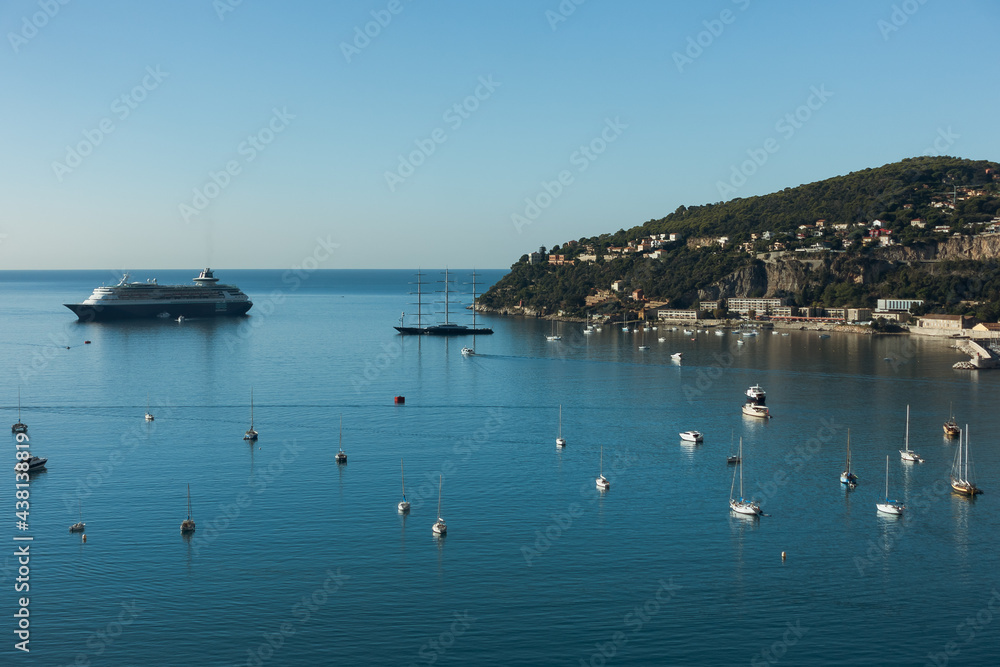 Aerial view of Mediterranean sea in french riviera. Blue sea with big cruise ship and small luxury yachts with small village on the hill at background on sunny summer day. High quality photo