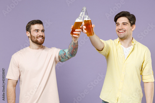 Two happy smiling cheeerful excited young men friends together 20s wearing casual t-shirt tattoo translate fun clink drink beer isolated on purple background studio portrait People lifestyle concept. photo