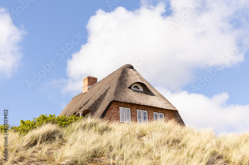 a Sylt typical brick house with a thatched roof. shot of special red houses with meadow and grass in the foreground.  photo