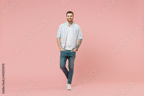 Full length young happy cheerful friendly caucasian unshaven man 20s in blue striped shirt white t-shirt look camera isolated on pastel pink color background studio portrait. People lifestyle concept.