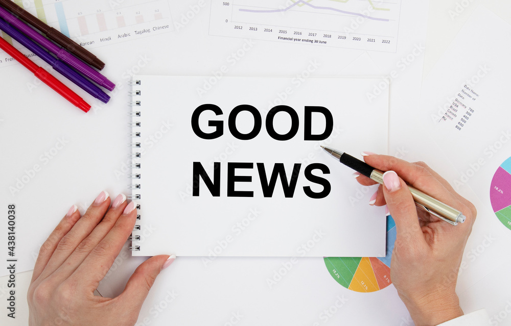 The girl holds a notebook with the text of Good News, next to pencils, diagrams and graphs. The girl holds a notebook with the text of Good News, next to pencils, diagrams and graphs.