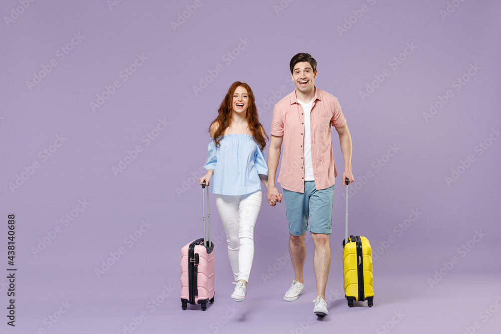 Full length two smiling traveler tourist woman man couple in shirt hold hand walk with suitcase isolated on purple background. Passenger travel abroad on weekends getaway. Air flight journey concept. Full length two smiling traveler tourist woman man couple in shirt hold hand walk with suitcase isolated on purple background. Passenger travel abroad on weekends getaway. Air flight journey concept.