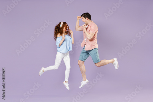 Full length traveler tourist woman man couple in shirt do winner gesture clench fist jump high isolated on purple background. Passenger travel abroad on weekends getaway. Air flight journey concept.